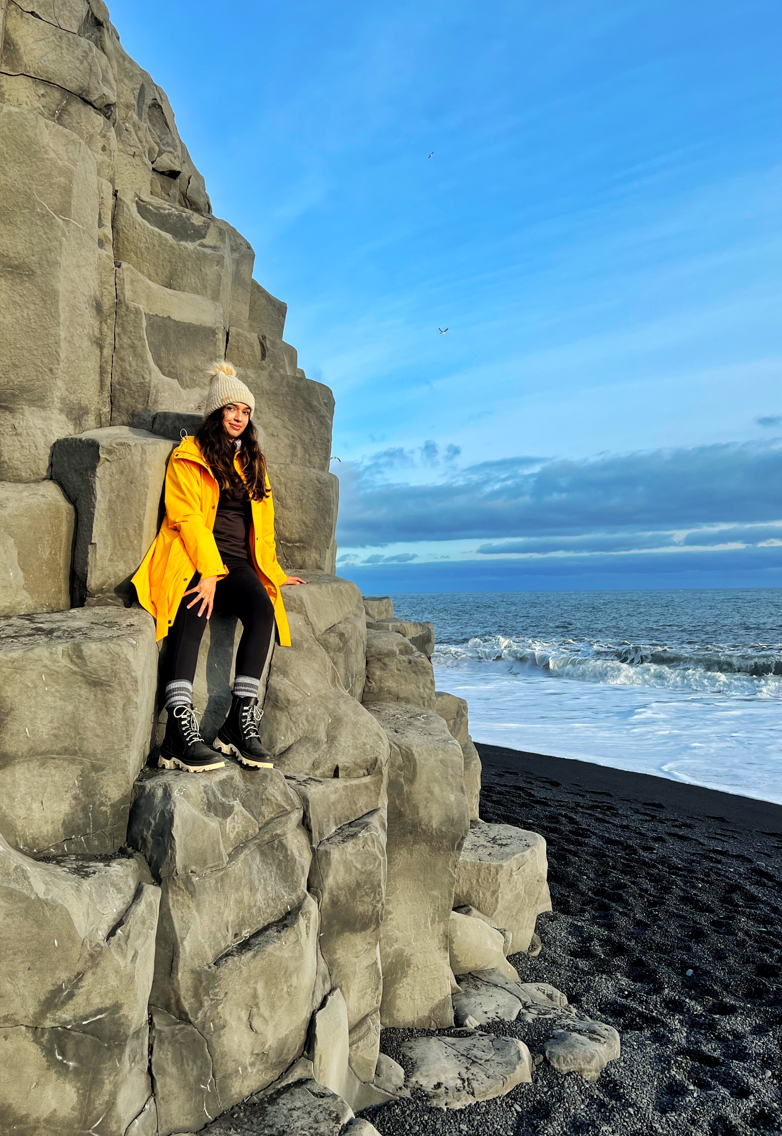 Kimberly Dsilva sitting on coastal rocks by the ocean.